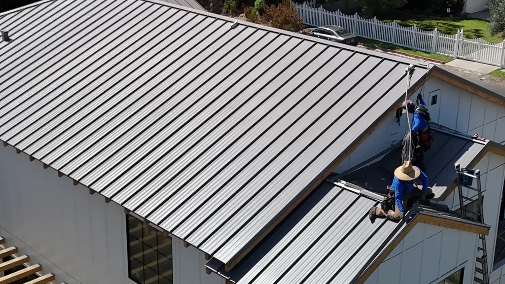 Two Eclipse Metal Roofing crew members setting standing seam panels on a white board-and-batten house