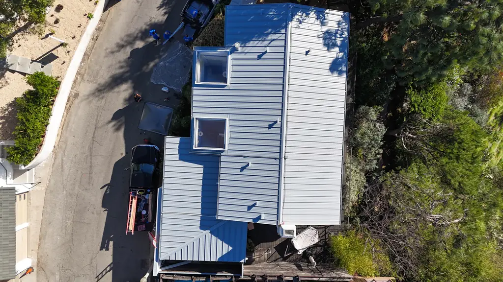Aerial view of a light gray standing seam roof with skylights on a hillside house