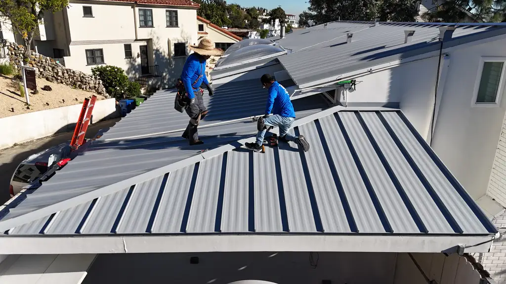 Two Eclipse Metal Roofing crew members installing light gray standing seam panels near skylights