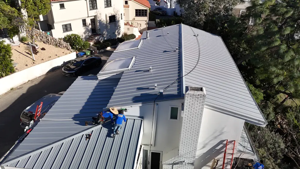Crew member installing standing seam panels around skylights on a hillside house