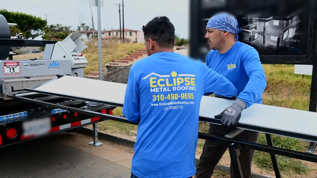 Two Eclipse Metal Roofing crew members guiding a freshly formed standing seam panel off a portable roll former
