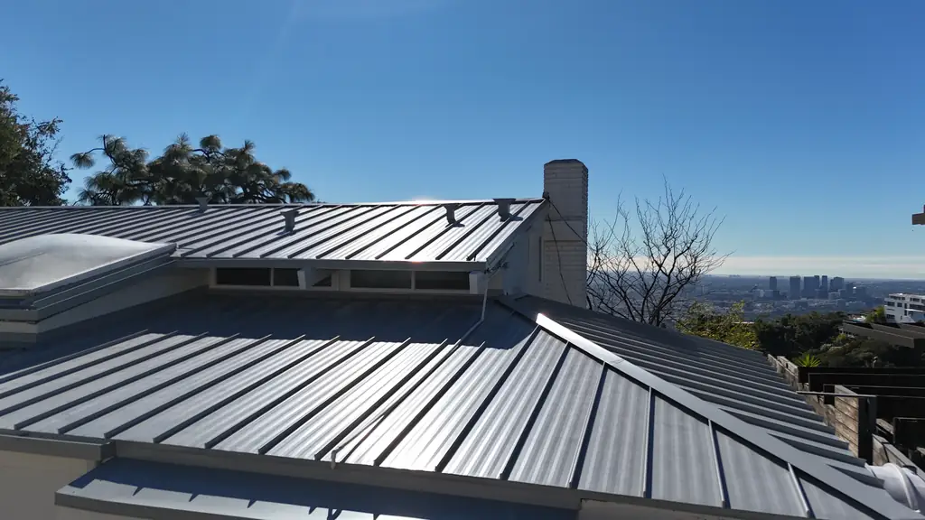 Charcoal standing seam metal roof with skylights, a chimney and a city skyline in the distance