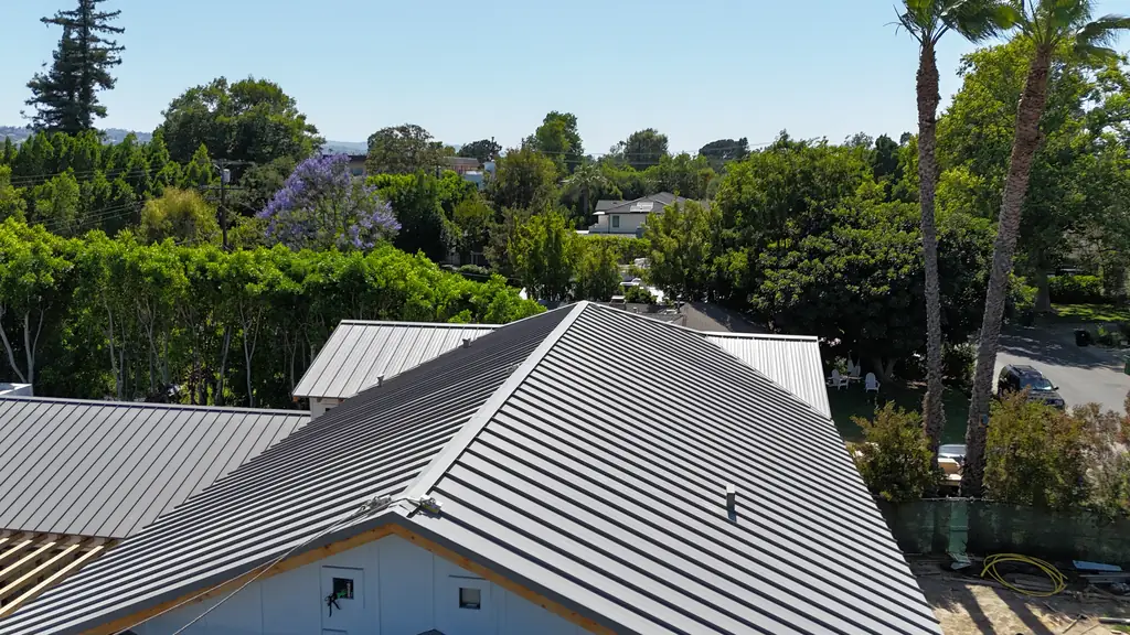 Gray standing seam metal roof on a white board-and-batten house surrounded by trees
