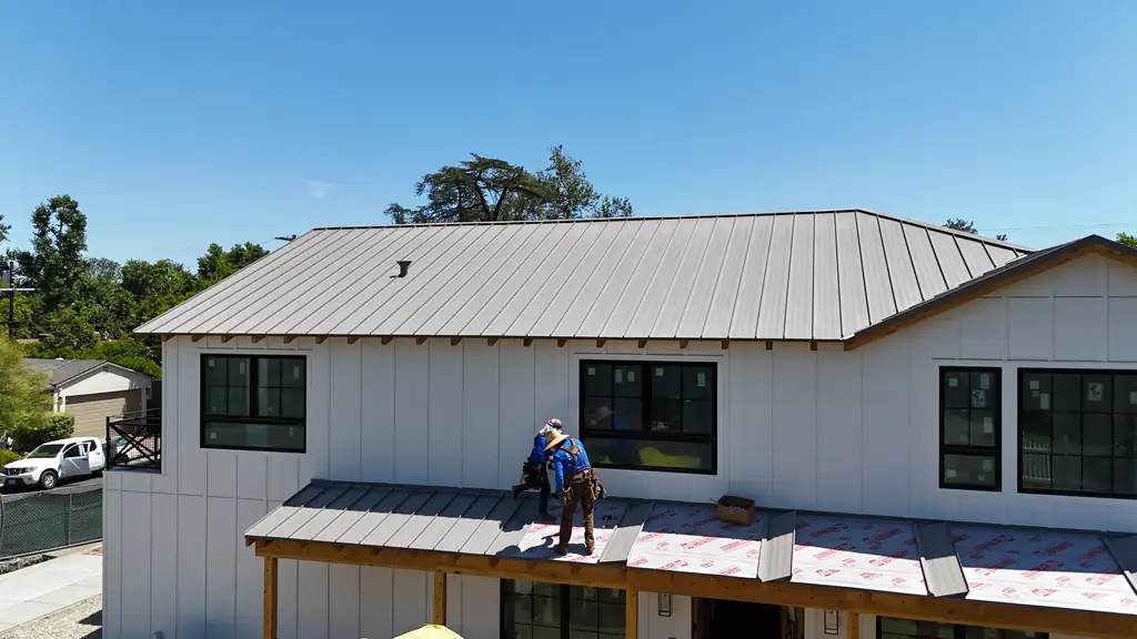 Gray standing seam roof on a white board-and-batten house, with a crew member finishing the porch roof